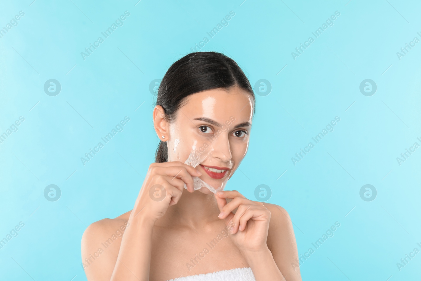 Photo of Smiling woman peeling off face mask on light blue background