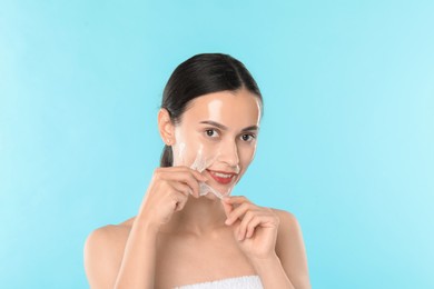 Photo of Smiling woman peeling off face mask on light blue background