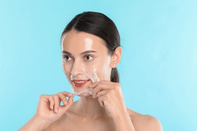 Photo of Smiling woman peeling off face mask on light blue background