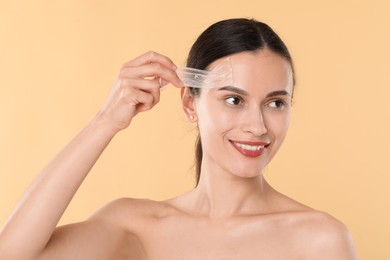 Photo of Smiling woman peeling off face mask on beige background