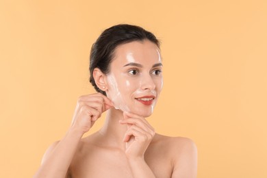 Beautiful woman peeling off face mask on beige background