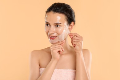 Photo of Smiling woman peeling off face mask on beige background