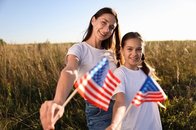 Happy mother and daughter with flags of USA outdoors, selective focus