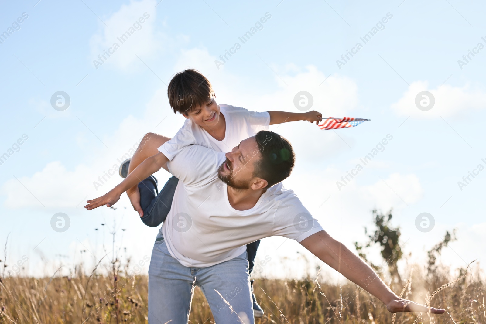 Photo of Happy father and son with flag of USA having fun outdoors