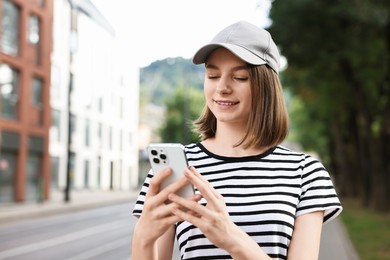 Photo of Portrait of smiling woman in baseball cap with smartphone outdoors. Space for text