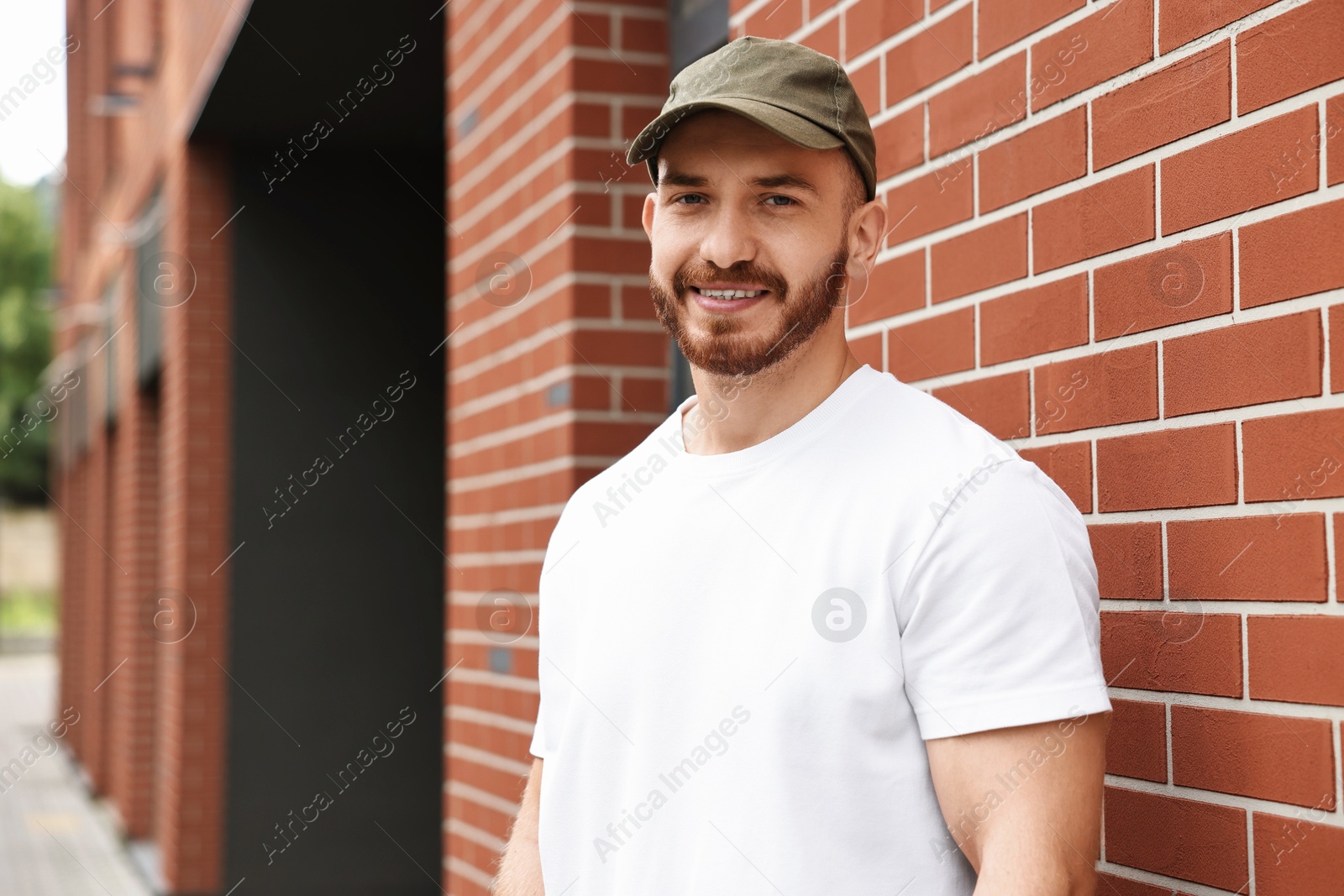 Photo of Portrait of smiling man in baseball cap near building outdoors. Space for text