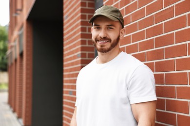 Portrait of smiling man in baseball cap near building outdoors. Space for text