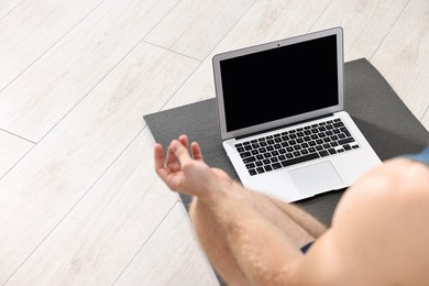 Man meditating near laptop on yoga mat at home, closeup. Space for text