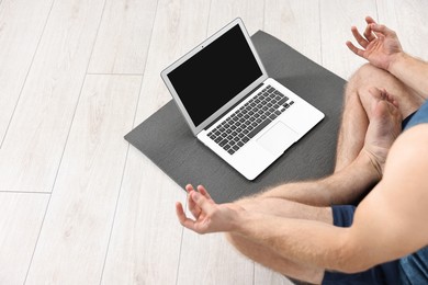 Photo of Man meditating near laptop on yoga mat at home, closeup. Space for text