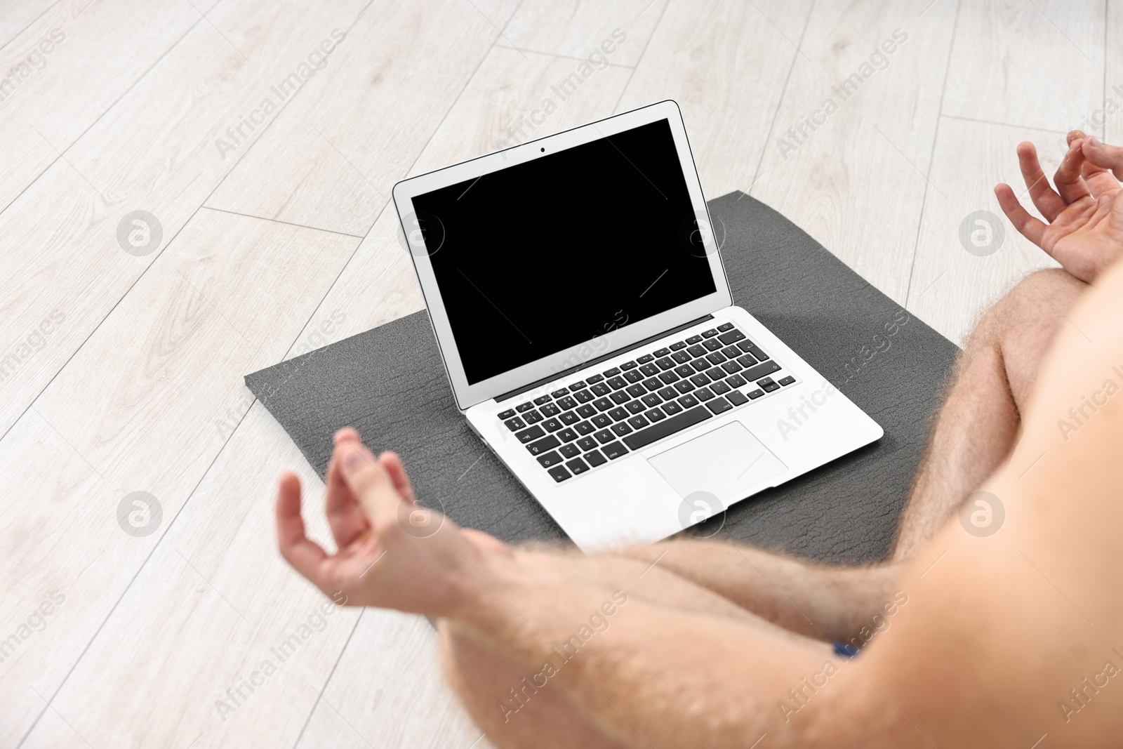 Photo of Man meditating near laptop on yoga mat at home, closeup. Space for text