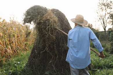 Photo of Senior man in straw hat pitching hay on farmland