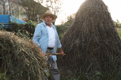 Photo of Senior man in straw hat pitching hay on farmland