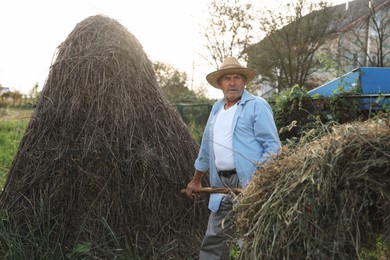 Photo of Senior man in straw hat pitching hay on farmland