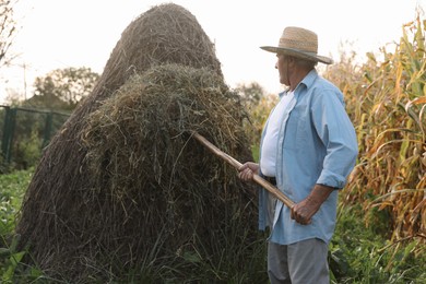 Senior man in straw hat pitching hay on farmland