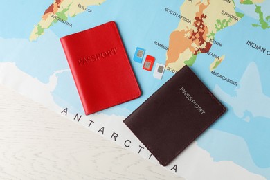 Photo of Passports, world map and SIM cards on white wooden table, flat lay