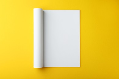 Open magazine with blank page on yellow background, top view. Mockup for design