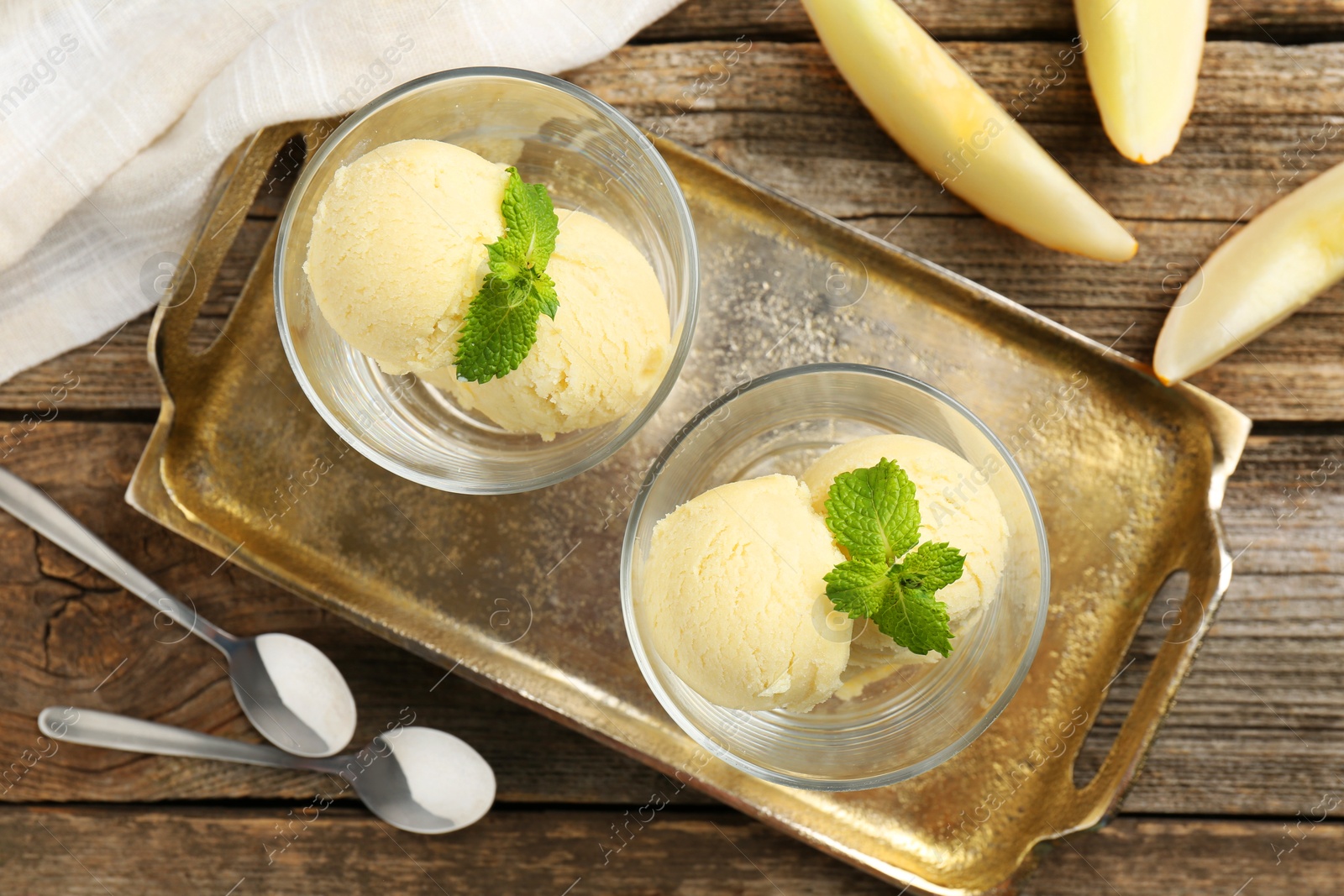 Photo of Scoops of melon sorbet with mint in glass dessert bowls, fresh fruit and spoons on wooden table, flat lay