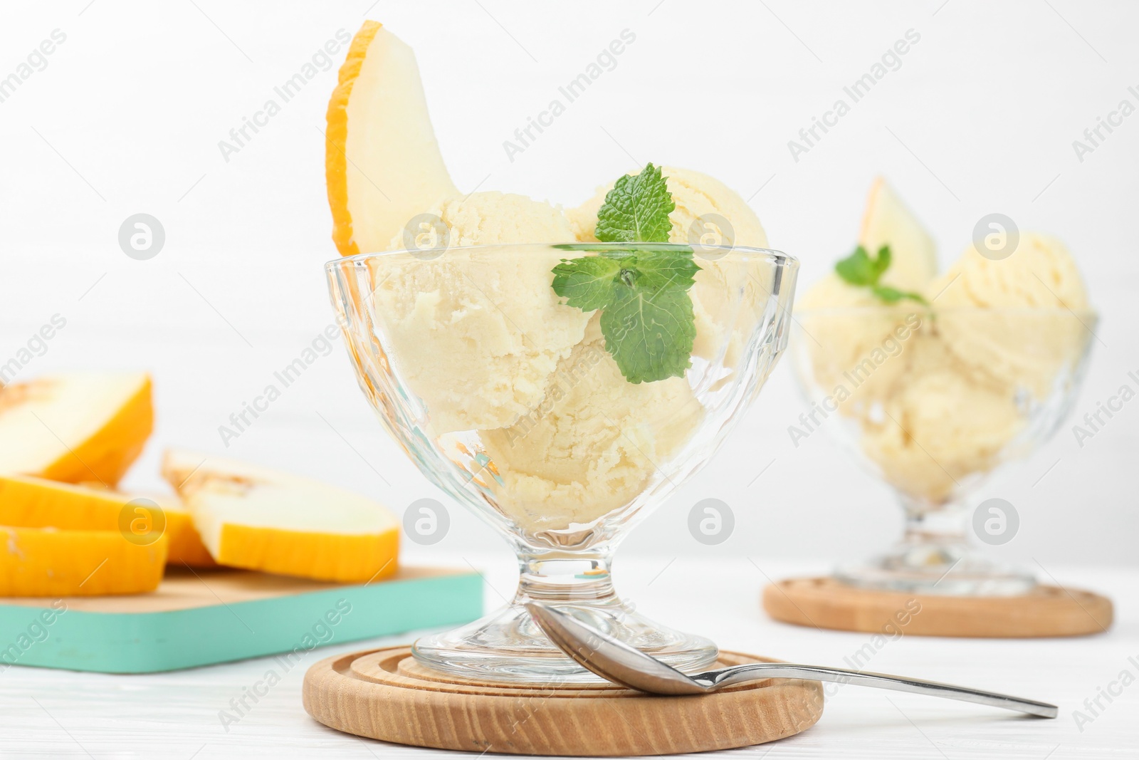 Photo of Scoops of melon sorbet with mint in glass dessert bowls and spoon on white wooden table, closeup