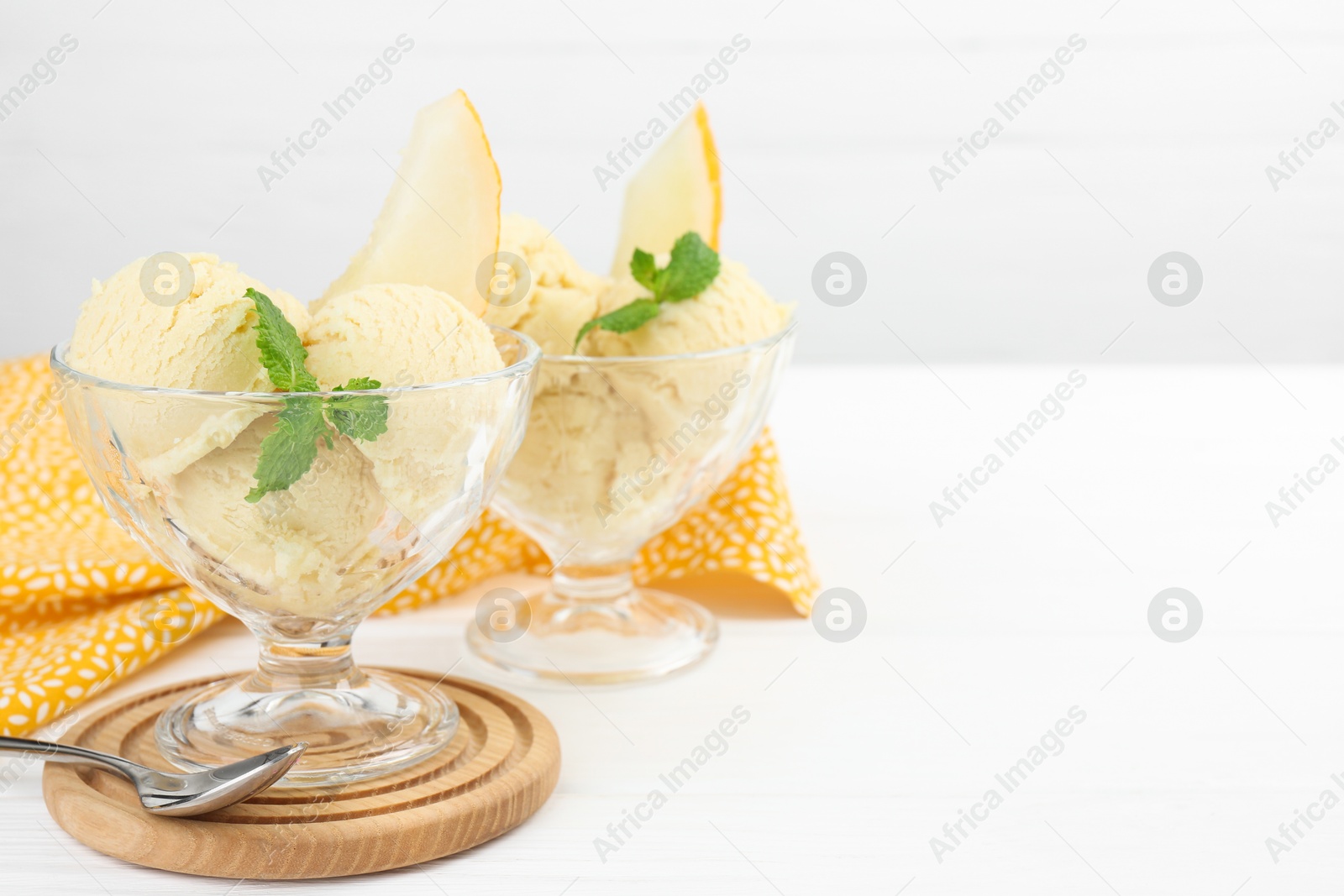 Photo of Scoops of melon sorbet with mint in glass dessert bowls and spoon on white wooden table, space for text