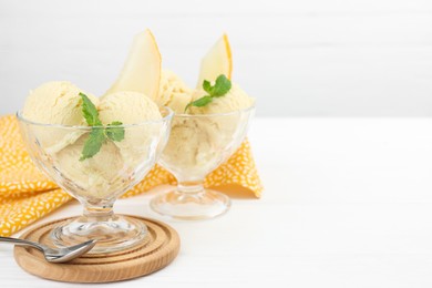 Photo of Scoops of melon sorbet with mint in glass dessert bowls and spoon on white wooden table, space for text