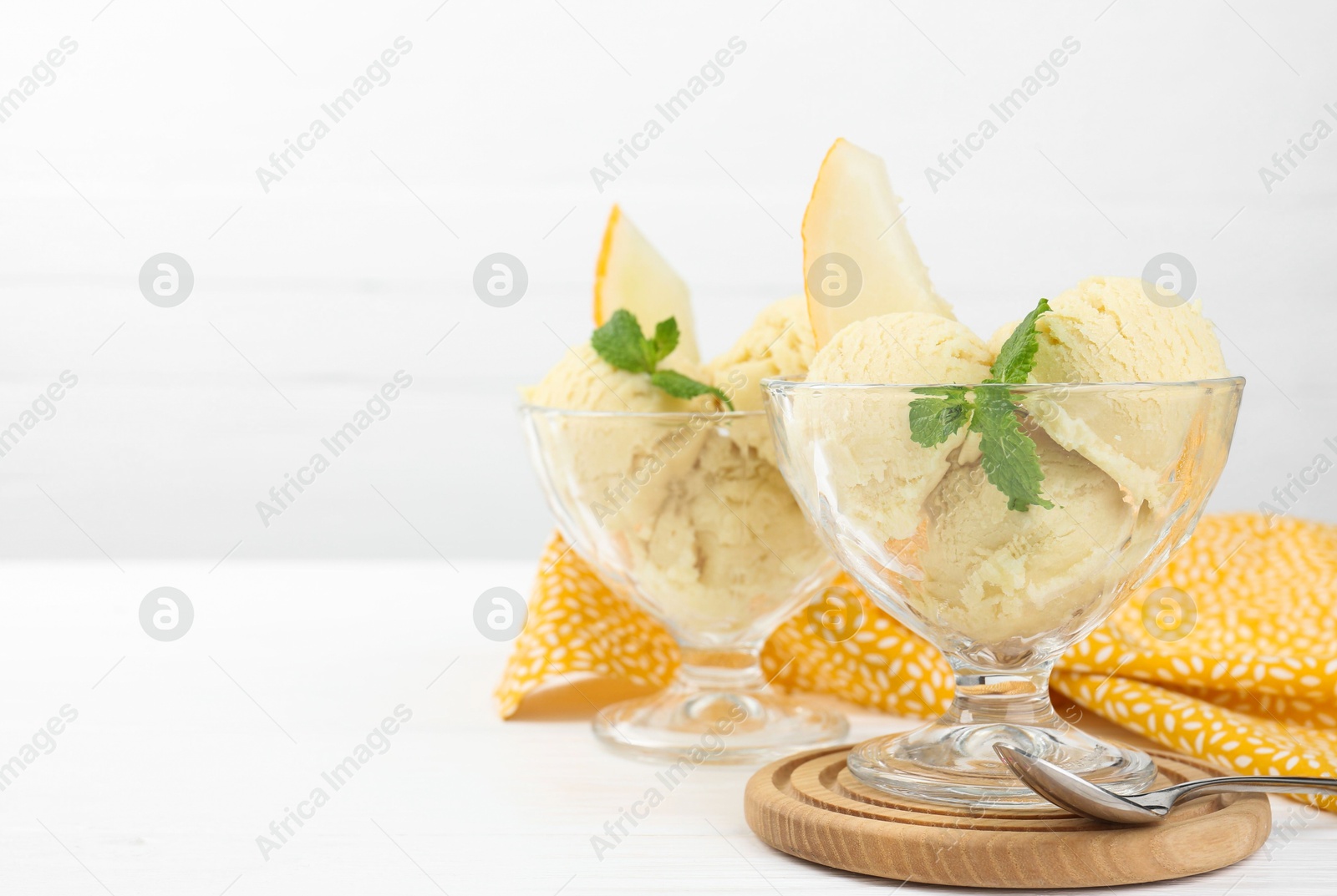 Photo of Scoops of melon sorbet with mint in glass dessert bowls and spoon on white wooden table, space for text