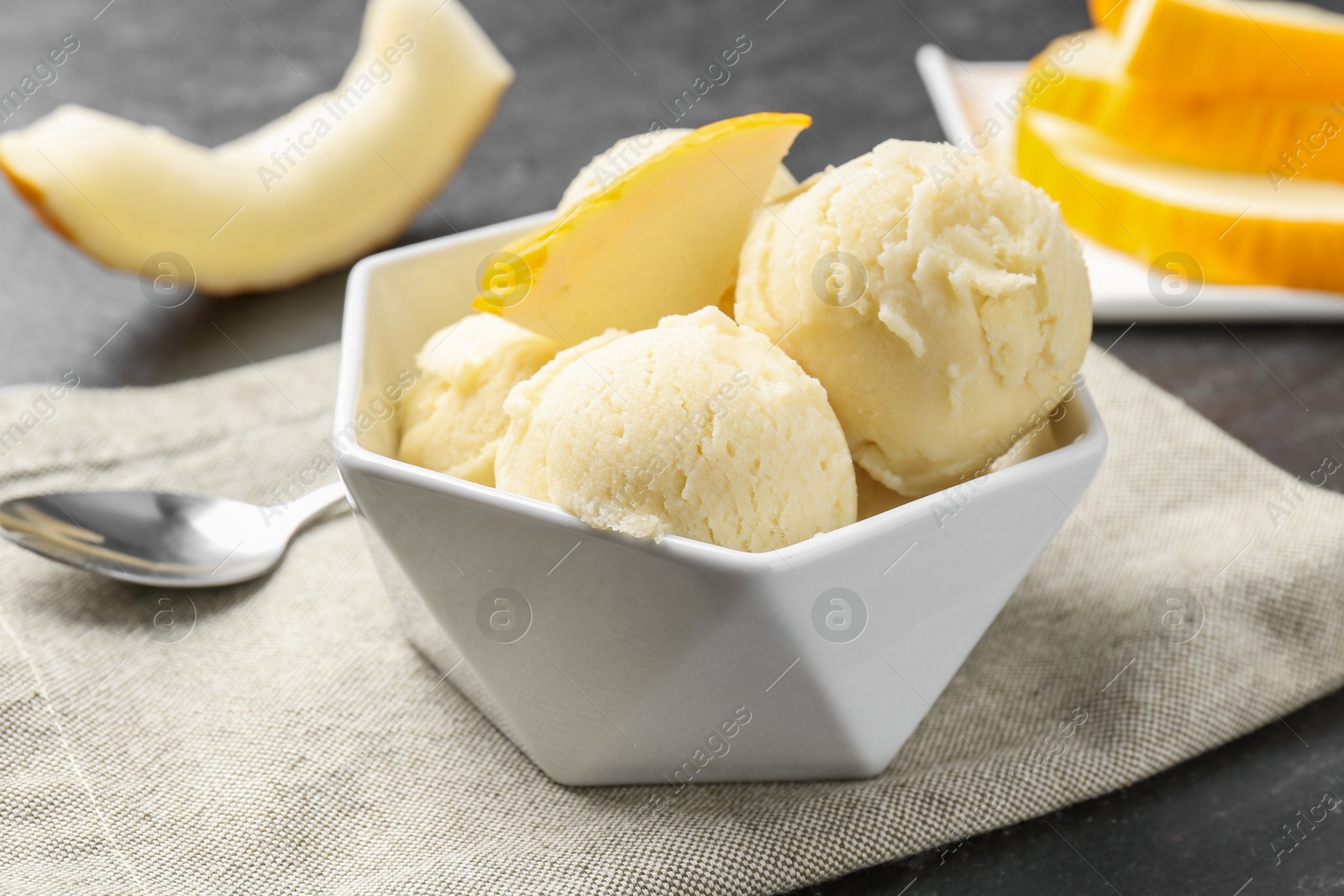 Photo of Scoops of tasty melon sorbet with fresh fruit in bowl on grey table, closeup