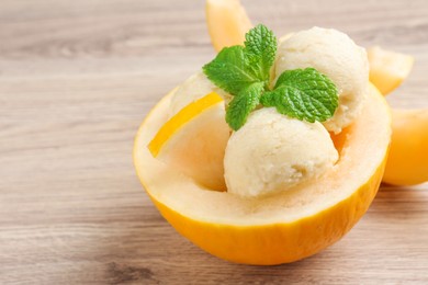 Photo of Scoops of tasty melon sorbet with mint in fresh fruit on wooden table, closeup