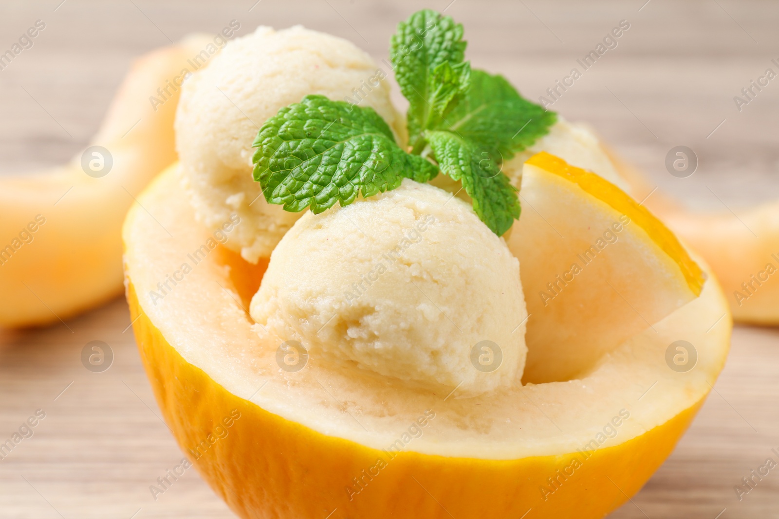 Photo of Scoops of tasty melon sorbet with mint in fresh fruit on wooden table, closeup