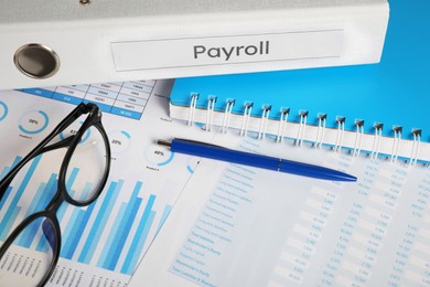 Photo of Payroll. Glasses, pen, notebook and graphical charts on table