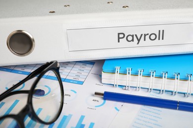 Photo of Payroll. Glasses, pen, notebook and graphical charts on table