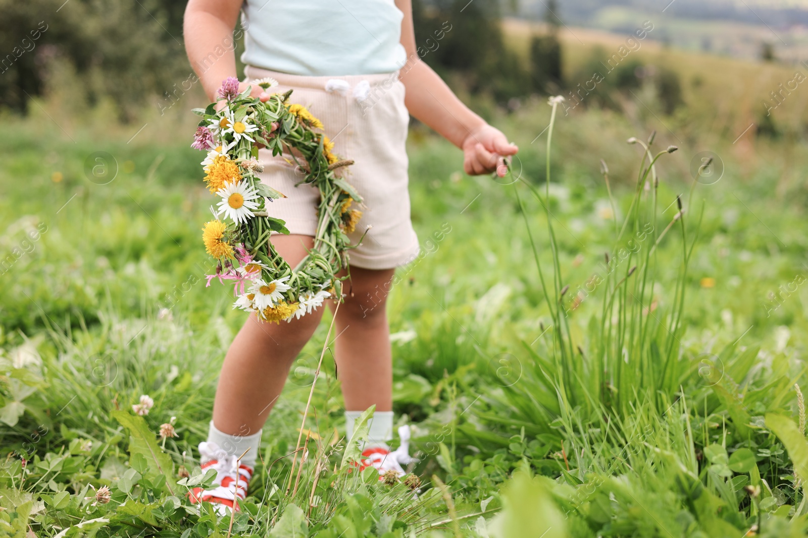 Photo of Little girl with floral wreath at meadow, closeup. Child enjoying beautiful nature