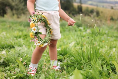 Photo of Little girl with floral wreath at meadow, closeup. Child enjoying beautiful nature