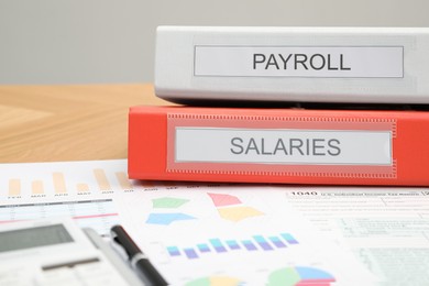 Payroll. Folders, charts, calculator and pen on wooden table, closeup