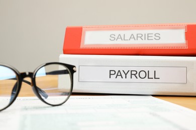 Photo of Payroll. Folders, glasses and form on wooden table, closeup