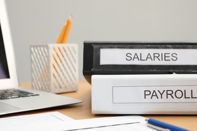 Photo of Payroll. Folders, documents and laptop on wooden table, closeup