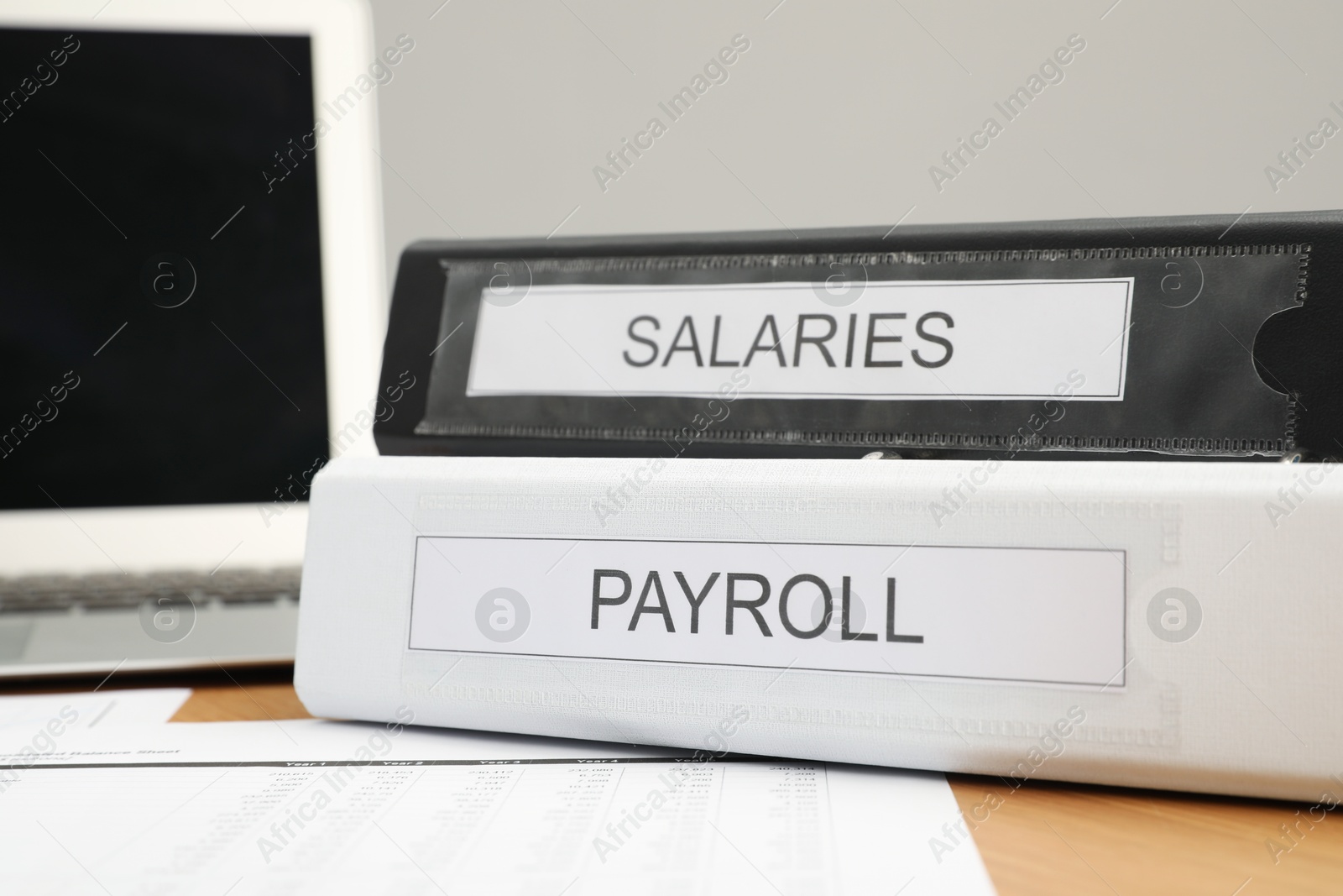 Photo of Payroll. Folders, documents and laptop on wooden table, closeup