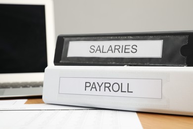 Photo of Payroll. Folders, documents and laptop on wooden table, closeup