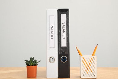 Photo of Folders with words Payroll and Salaries, houseplant and holder with pencils on wooden table