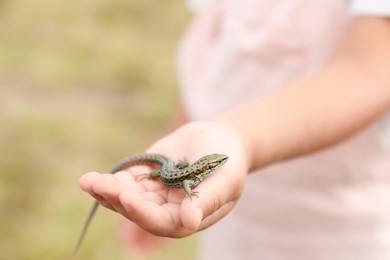 Little girl holding lizard on blurred background, closeup, space for text. Child enjoying beautiful nature