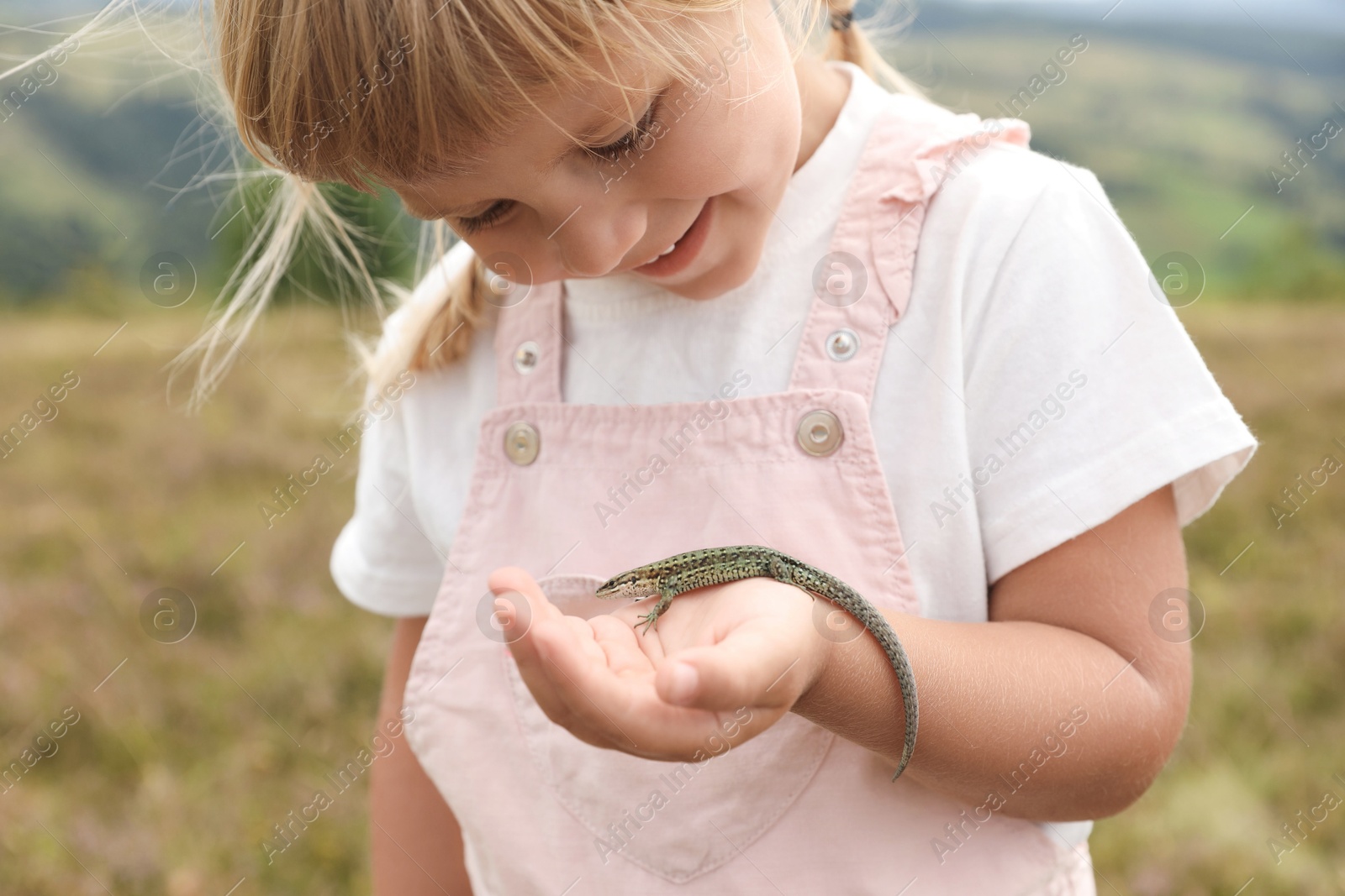 Photo of Smiling little girl holding lizard at field. Child enjoying beautiful nature