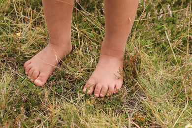 Photo of Little girl standing barefoot outdoors on sunny day, closeup. Child enjoying beautiful nature