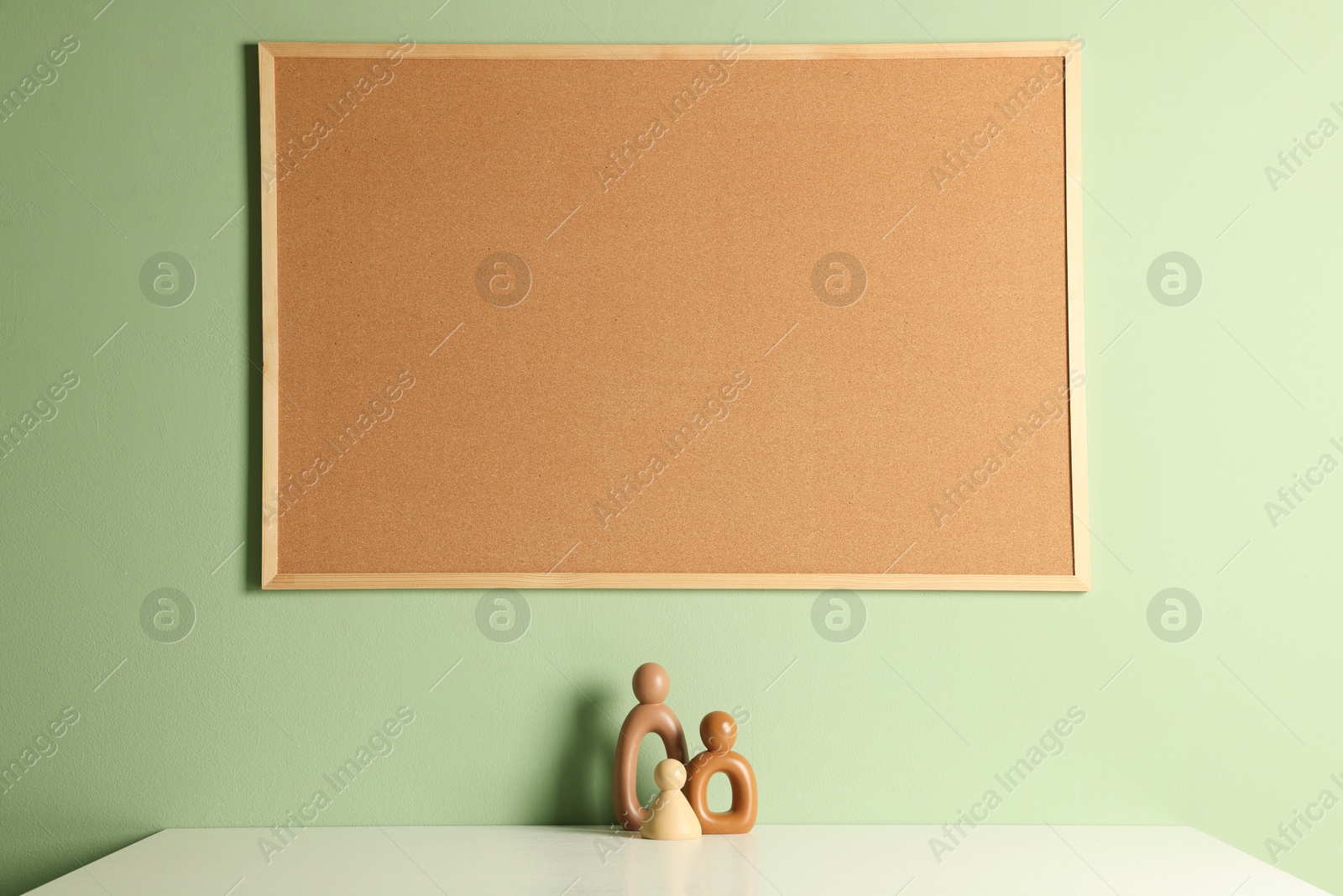 Photo of Cork board and decorative figures on light table near green wall indoors