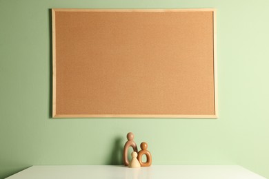 Photo of Cork board and decorative figures on light table near green wall indoors