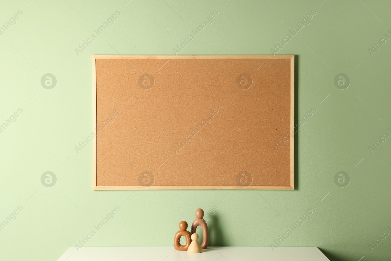 Photo of Cork board and decorative figures on light table near green wall indoors