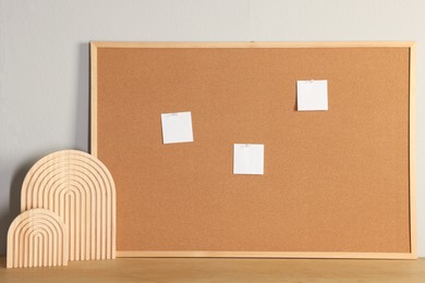 Cork board with blank paper notes and decorative elements on wooden table near light wall