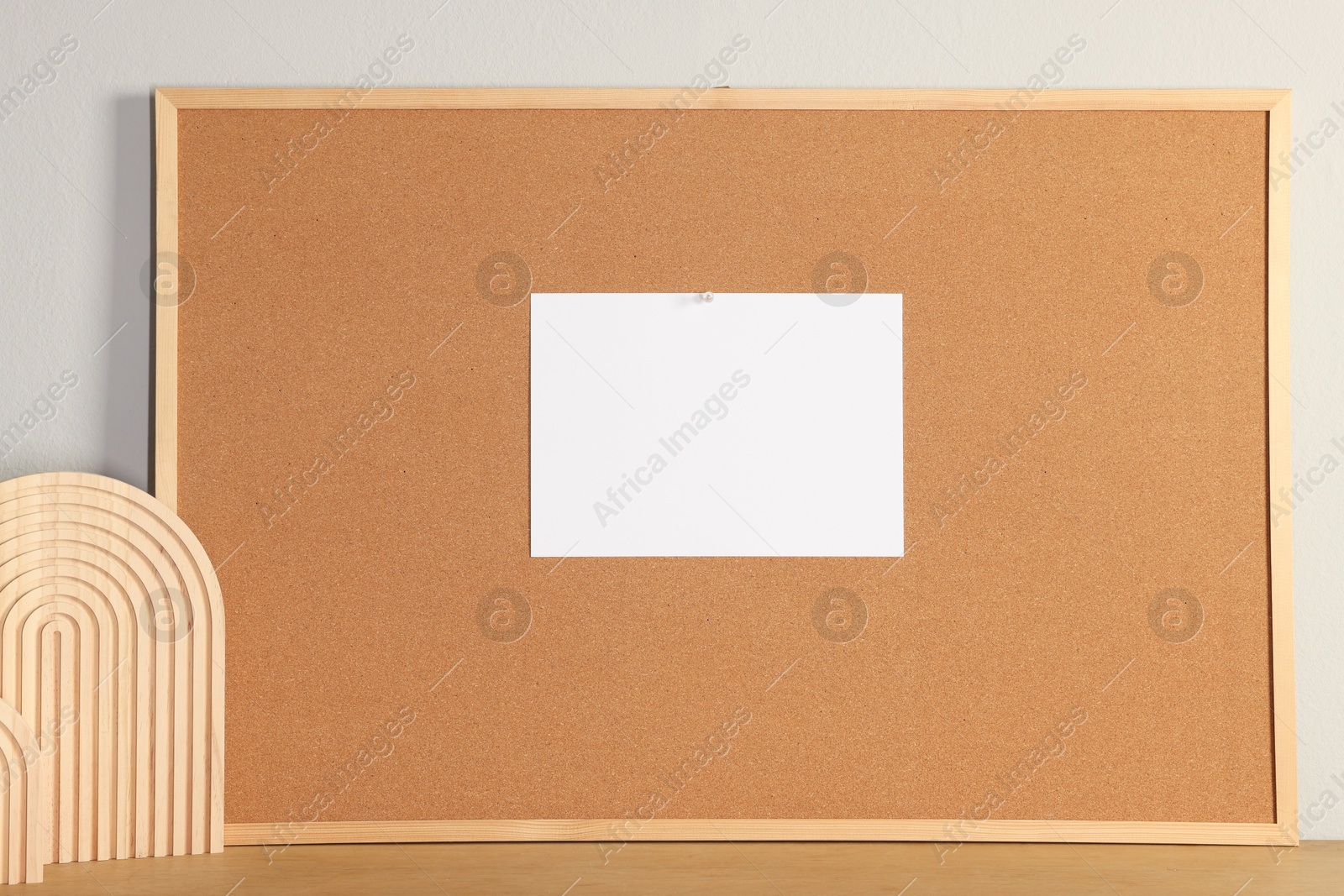 Photo of Cork board with blank paper note and decorative elements on wooden table near light wall