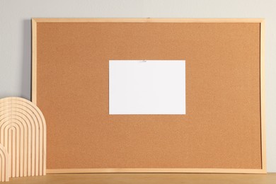 Cork board with blank paper note and decorative elements on wooden table near light wall