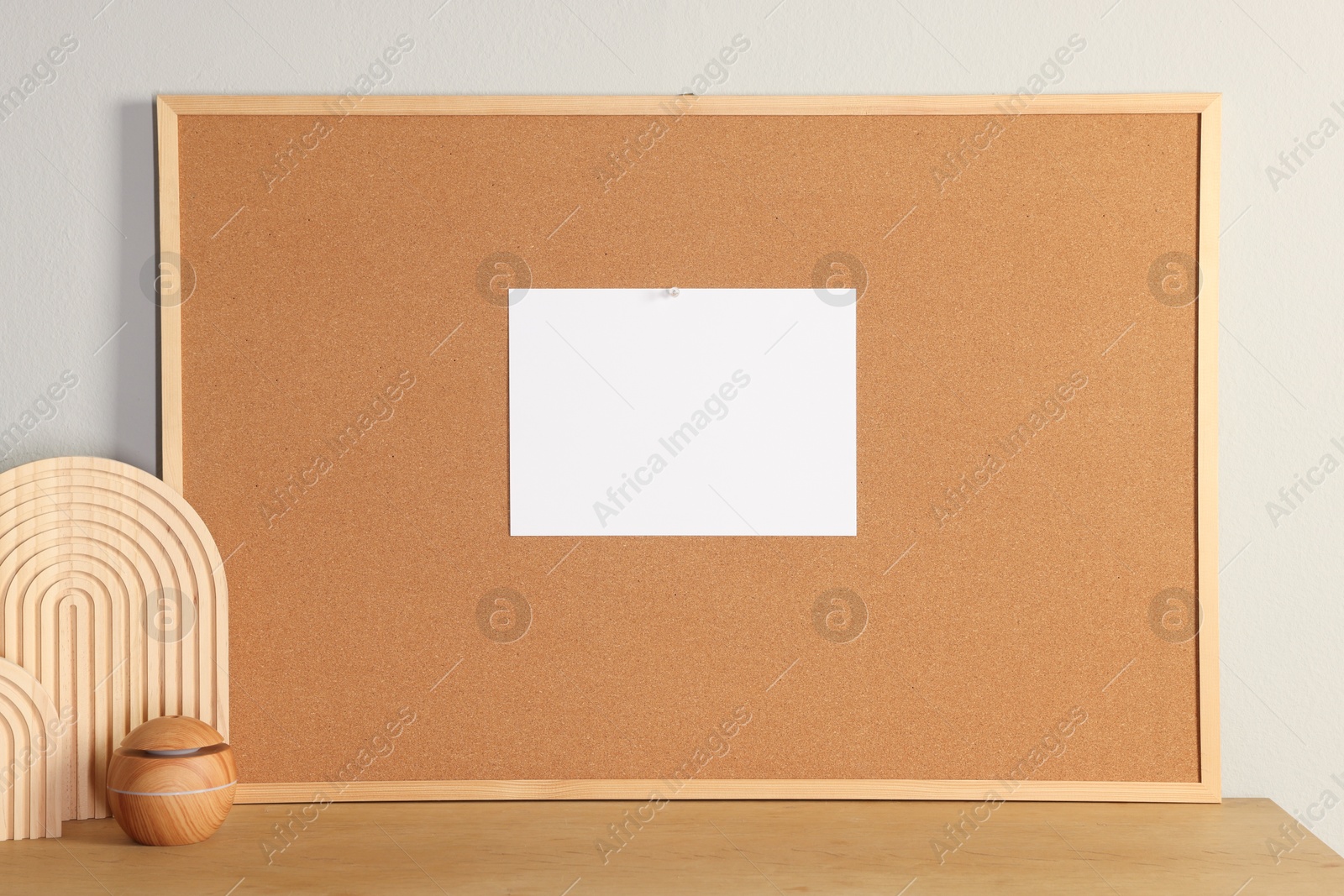 Photo of Cork board with blank paper note and decorative elements on wooden table near light wall