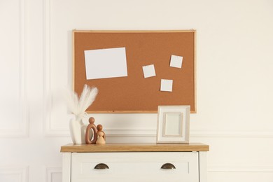 Photo of Cork board with blank paper notes and decorative elements on chest of drawers