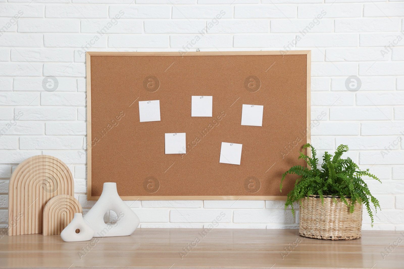 Photo of Cork board with blank paper notes and decorative elements on wooden table near white brick wall